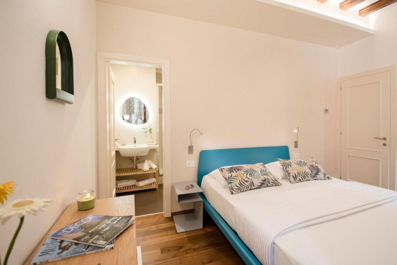 Ein Schlafzimmer mit einem Bett, einem Nachttisch, einem Spiegel, einem Regal und einer Tür.