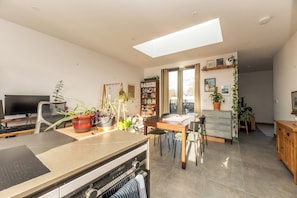 A modern kitchen with a dining area, a TV, and a bookshelf.