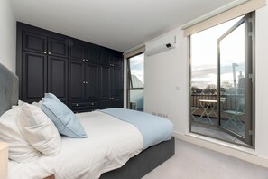 A bedroom with a large bed, dark cabinets, a sliding glass door to a balcony, and a city view. - Beautiful 1BR, Huge Terrace 17 mins central London - Pass the Keys (Surbiton)