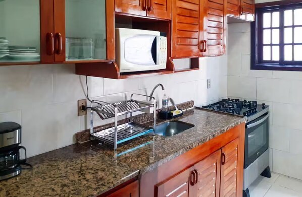 Una cocina con armarios de madera, microondas, escurreplatos, estufa y cafetera.