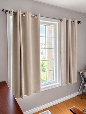 A room with a window, beige curtains, a wooden desk, and a chair.