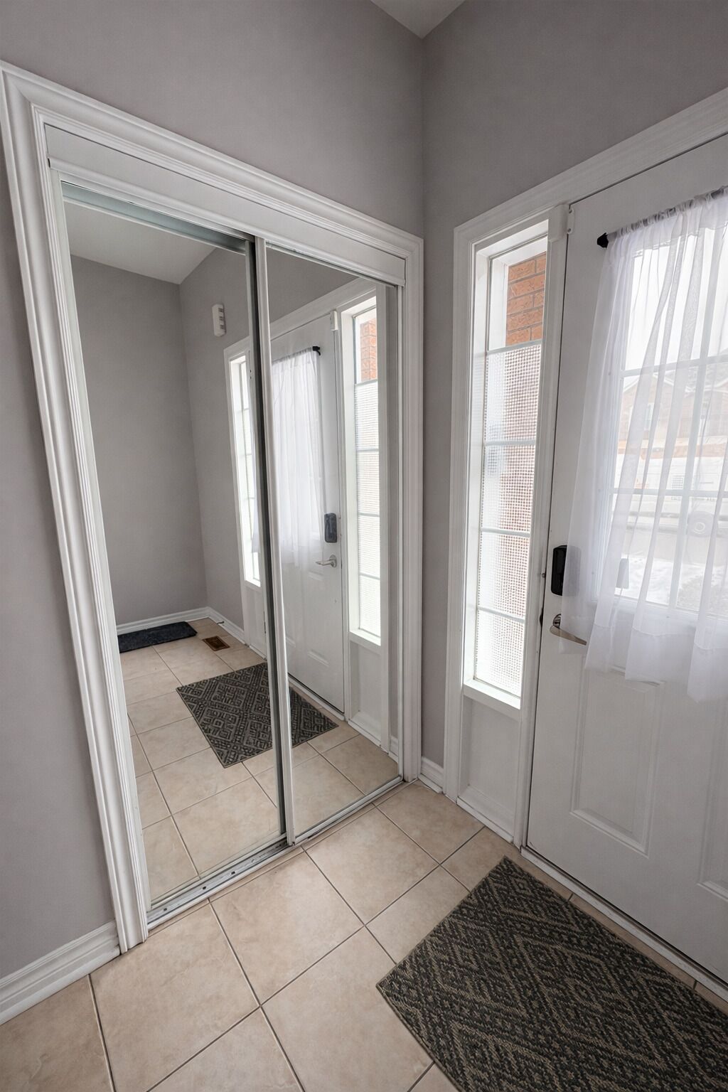 A room with a sliding glass door, a door with a curtain, and a patterned rug on the floor.