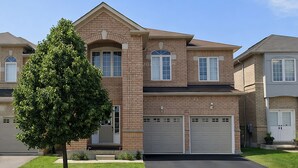 A two-story house with a brick facade, a central entrance, and a driveway leading to a garage. - Private Queen Bed w/Mini Fridge, 2.5 Baths—Brampton Shared Home near GO Station! (Brampton)