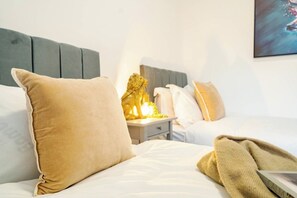 A hotel room with a bed, pillows, a nightstand, and a decorative golden statue. - Modern 3 Bedroom House | WA10 | Central St. Helens (St Helens)