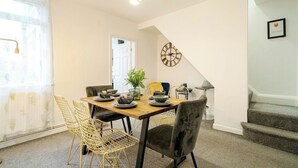 A dining area with a wooden table, chairs, and a clock on the wall. - Modern 3 Bedroom House | WA10 | Central St. Helens (St Helens)