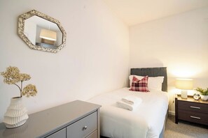 Een slaapkamer met een bed, een nachtkastje met een lamp, een dressoir en een spiegel aan de muur.