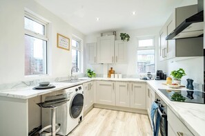 Une cuisine moderne avec des meubles blancs, un lave-linge encastré et une grande fenêtre.
