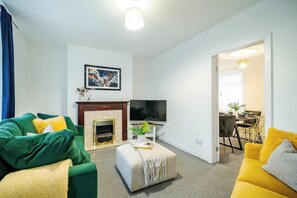 Ein Wohnzimmer mit Kamin, Fernseher und einem Essbereich, der durch eine geöffnete Tür sichtbar ist.