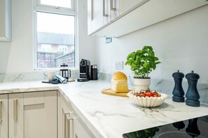 Une cuisine avec un plan de travail en marbre, une miche de pain, une plante en pot, un saladier de tomates et deux moulins à poivre.