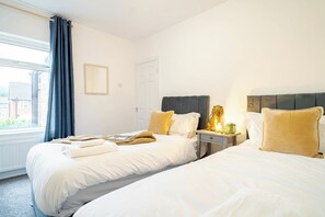 Ein Hotelzimmer mit zwei Betten, einem Fenster mit Vorhängen, einem Nachttisch mit Lampe und einer Tür.