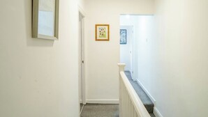A hallway with a door at the end, a framed quote on the wall, and a small framed picture. - Modern 3 Bedroom House | WA10 | Central St. Helens (St Helens)