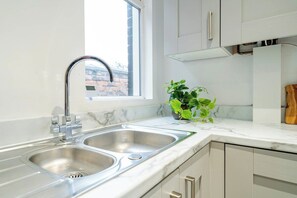 Een moderne keuken met een dubbele spoelbak, een witte marmeren aanrechtblad en een raam met uitzicht op een bakstenen gebouw.