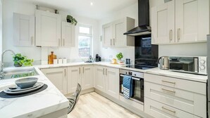 A modern kitchen with white cabinetry, a black range hood, and a built-in oven. - Modern 3 Bedroom House | WA10 | Central St. Helens (St Helens)