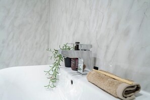 Ein Badezimmer mit Marmorwand, einem Waschbecken, einer Handseifenflasche, einem Handtuch und einer Pflanze.
