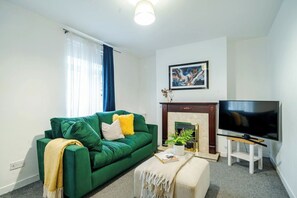 Ein Wohnzimmer mit einem grünen Sofa, einem Flachbildfernseher, einem Kamin und einem Gemälde an der Wand.