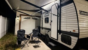 A Coleman RV parked at night with a covered patio area, two chairs, and a table.