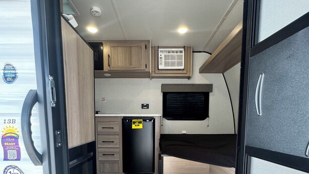 A compact RV kitchen with wooden cabinets, a black refrigerator, and a window above the sink.