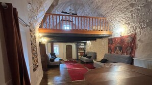 A cozy attic room with a wooden table, a red carpet, and a loft area with a wooden railing. - Lou Castel - Medieval castle (Le Clapier)