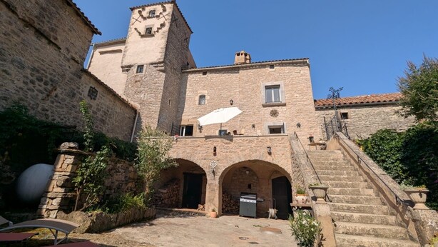 A stone building with a tower, arched doorways, and a staircase leading to the upper levels. - Lou Castel - Medieval castle (Le Clapier)