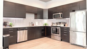 Une cuisine moderne avec des meubles de couleur sombre, des appareils en acier inoxydable et un plancher en bois clair.