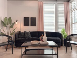 A modern living room with a black sofa, a glass coffee table, and a large potted plant.
