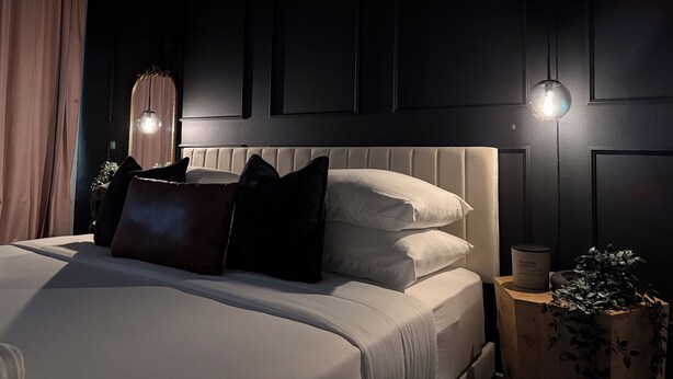 Une chambre à coucher avec un lit, des oreillers, une table de chevet avec une bougie et un luminaire fixé au mur.