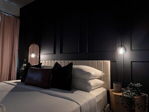 A bedroom with a bed, pillows, a bedside table with a candle, and a wall-mounted light fixture.