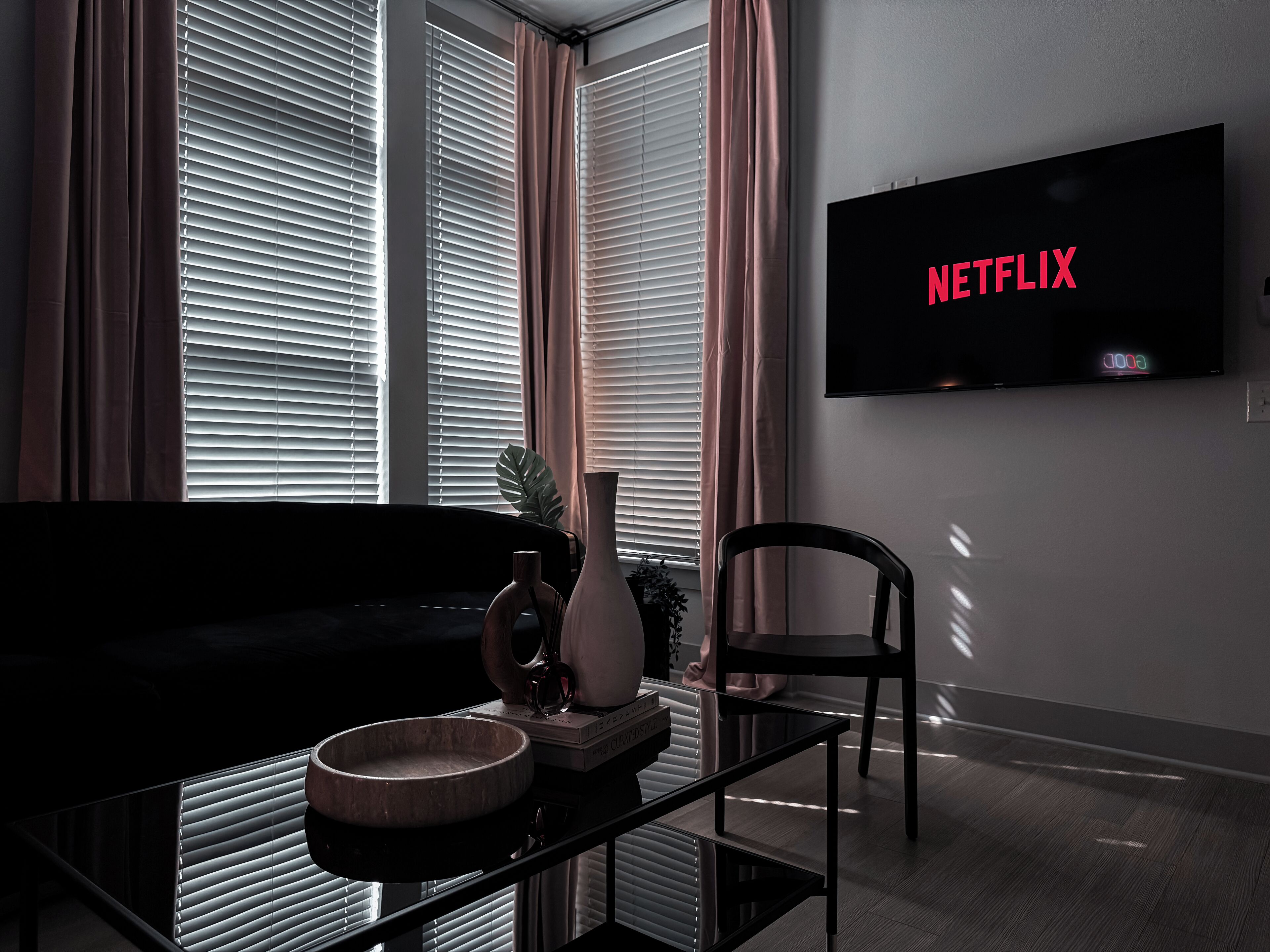 Un salon moderne avec un canapé noir, une table basse en verre et un téléviseur affichant le logo « NETFLIX ».