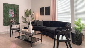Un salon moderne avec un canapé noir, une table basse en verre et un élément de décoration murale vert.