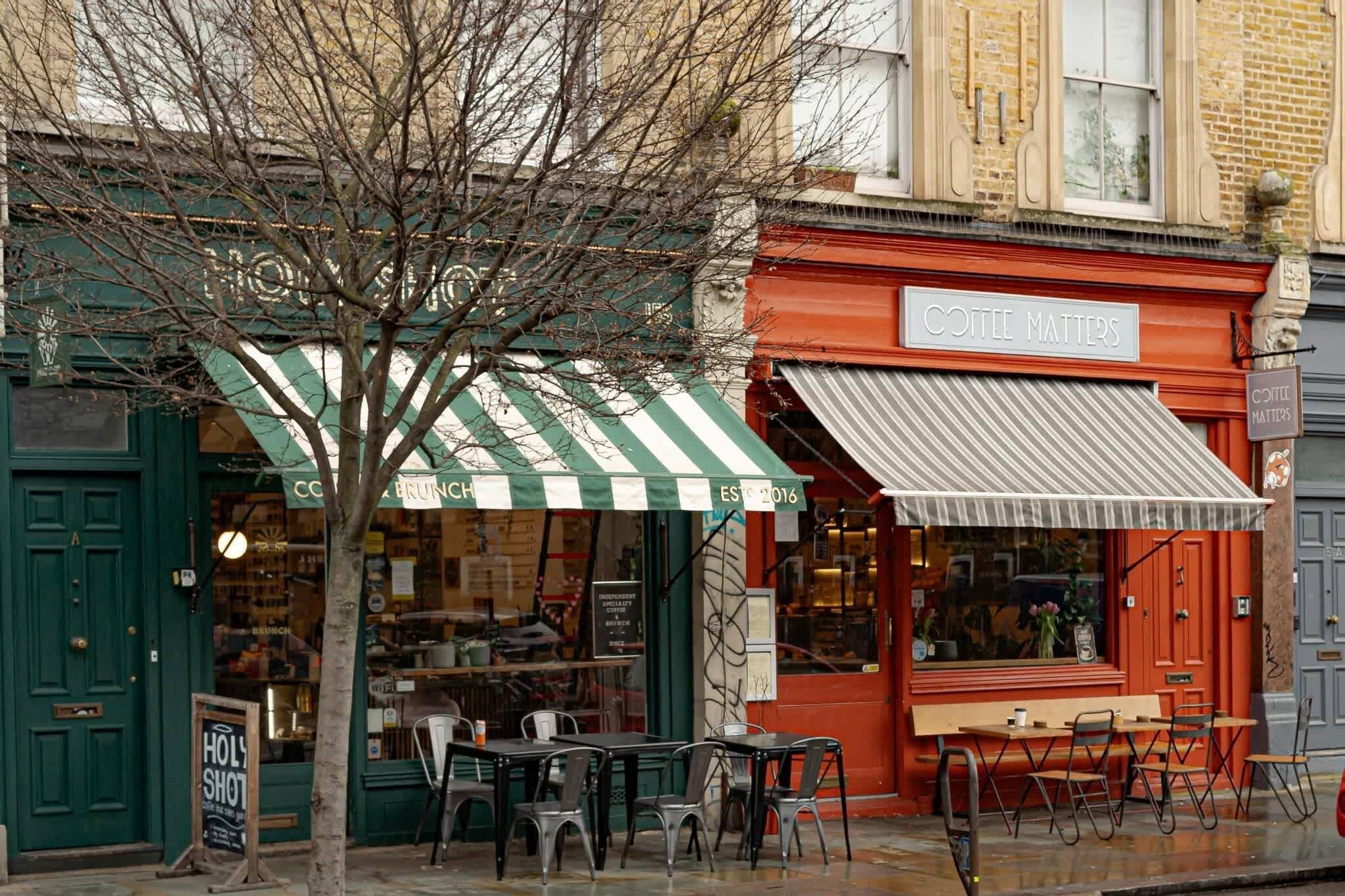 Un café avec une terrasse, une enseigne indiquant qu’il s’agit d’un café, et un arbre devant.