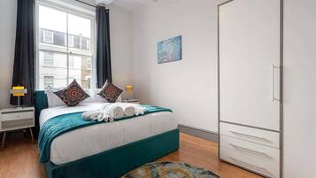 A hotel room with a bed, a nightstand, a lamp, a wardrobe, and a view of the outside.
