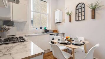 A modern kitchen with white cabinetry, a marble countertop, and a dining area with white chairs.