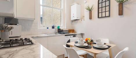 A modern kitchen with white cabinetry, a marble countertop, and a dining area with white chairs.