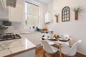 Une cuisine moderne avec des meubles blancs, un plan de travail en marbre et un coin repas avec des chaises blanches.