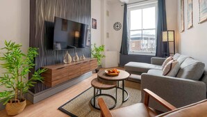 Een moderne woonkamer met een flatscreen televisie, een bank, een salontafel en decoratieve planten.