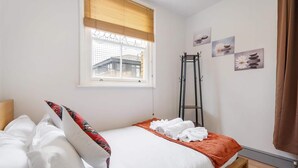 Un dormitorio con cama, ventana con persianas, escalera y decoración en la pared.