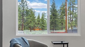 A room with a grey armchair, a small black table, and a window with a view of trees and a clear sky. - Modern 1BR: Walk to Heavenly, Beach, Ski, Golf & Casinos: Pet Friendly (South Lake Tahoe)