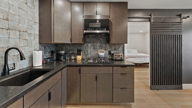 Une cuisine moderne avec des meubles de couleur sombre, une hotte en acier inoxydable, une cuisinière à gaz et un grille-pain.
