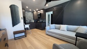 Un salon moderne avec un canapé, un coin repas avec une cuisine en arrière-plan, un ventilateur de plafond et un plancher en bois.