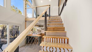 Een moderne trap met houten treden en een houten leuning, die leidt naar een hoger gelegen deel met grote ramen.