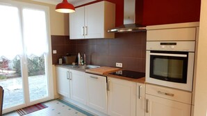 Une cuisine avec des armoires blanches, un luminaire suspendu rouge, un four encastré et une grande fenêtre donnant sur l’extérieur.