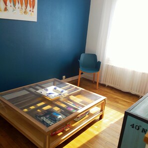 A room with a glass-top table, a blue chair, and a window with white curtains.