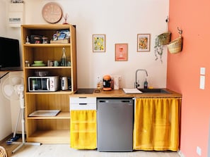 A compact kitchen with a microwave, toaster, and coffee maker. There are two sinks, a dishwasher, and a wooden shelf with kitchen items. - Cosy studio with garden - "Le Luhana (Luzillé)