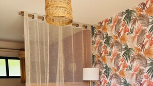 Un salon chaleureux avec un canapé, une table à manger et un mur recouvert d’un papier peint aux motifs tropicaux.