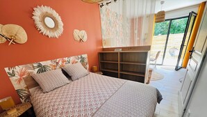 Une chambre avec une couvre-lit à motifs, une tête de lit en bois, une table de chevet, un miroir et une vue sur une terrasse extérieure.