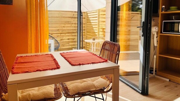 Un coin repas avec une table et des chaises, une porte vitrée donnant sur l’extérieur et une clôture en bois visible à travers la porte.