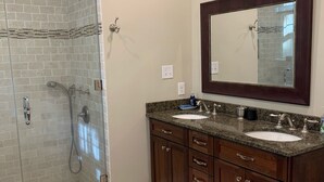 A bathroom with a glass shower enclosure, a double sink vanity, and a large mirror above the vanity.