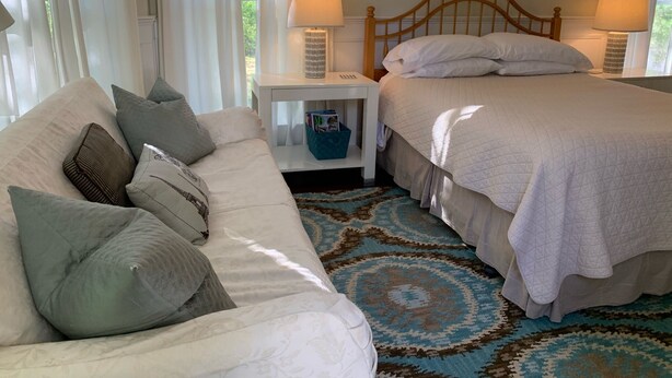 A bedroom with a bed, a nightstand, a lamp, a framed picture on the wall, and a window with curtains.