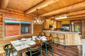 A wooden cabin interior with a dining area, kitchen, and bar.