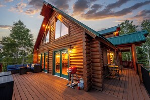 A log cabin with a deck, outdoor seating, and a barbecue grill.